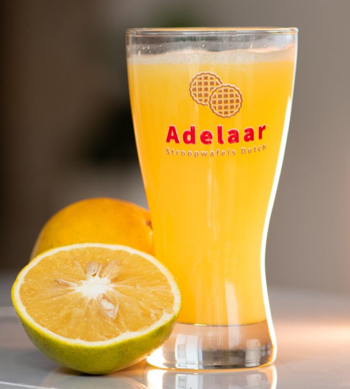 Vaso de jugo de naranja recién exprimido junto a un stroopwafel